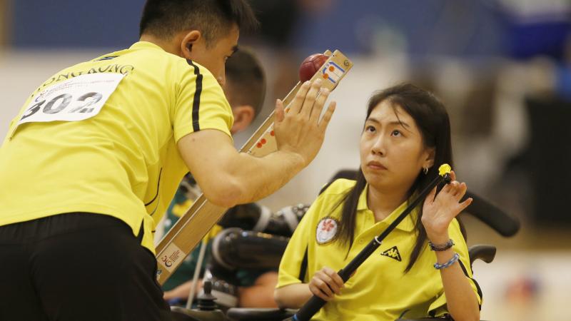 female boccia player Ho Yuen Kei listens to her coach before taking a shot