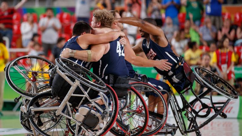 a group of male wheelchair basketballers from the USA hug on the court