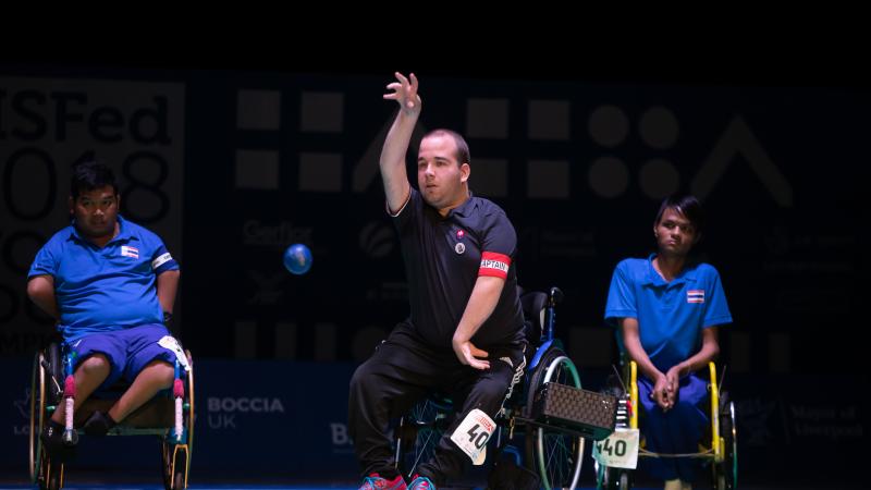 Men in a wheelchair throwing a blue ball observed by other two men
