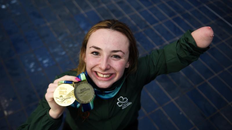 female Para swimmer Ellen Keane smiles and holds up her gold medal