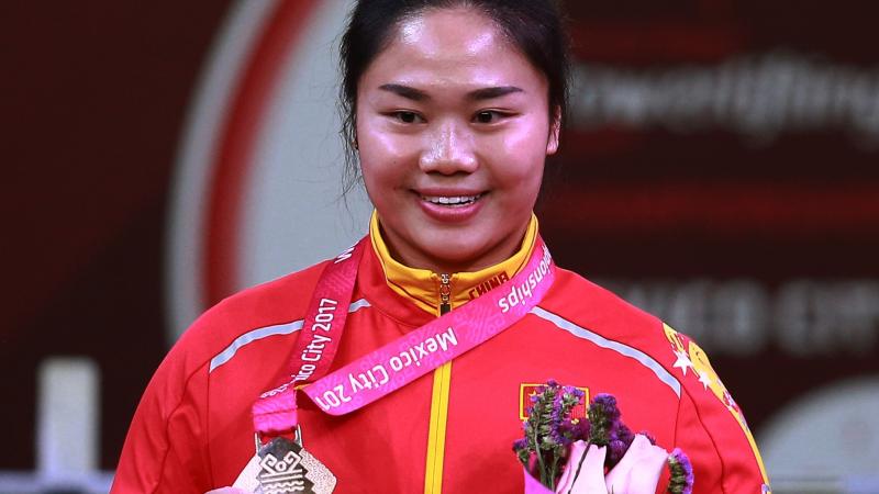 Yujiao Tan female powerlifter Yujiao Tan holds up her gold medal and a bunch of flowers