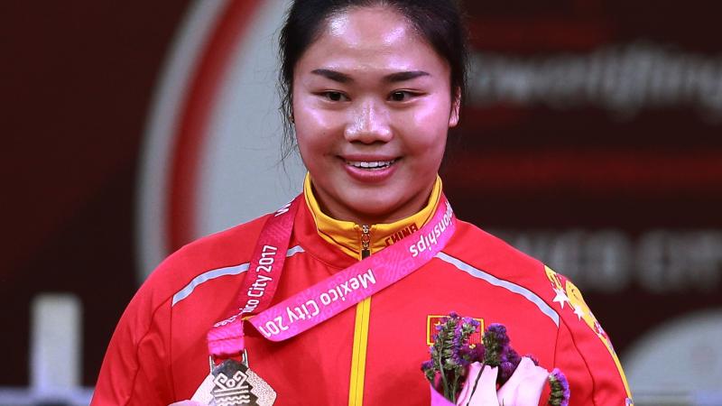 female powerlifter Yujiao Tan holds up her gold medal and a bunch of flowers