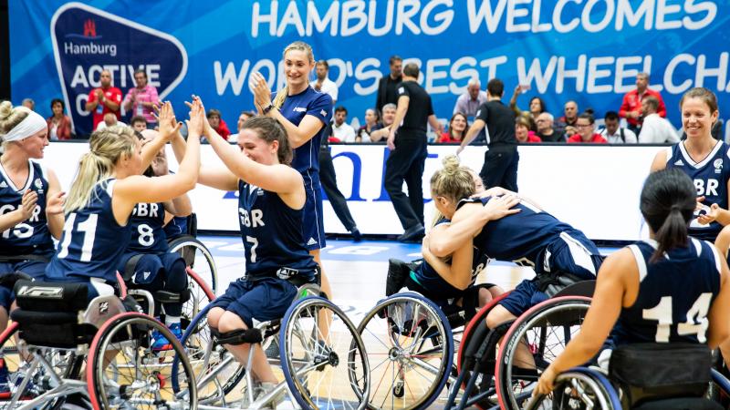 a group of female British wheelchair basketballers hugging and smiling on court