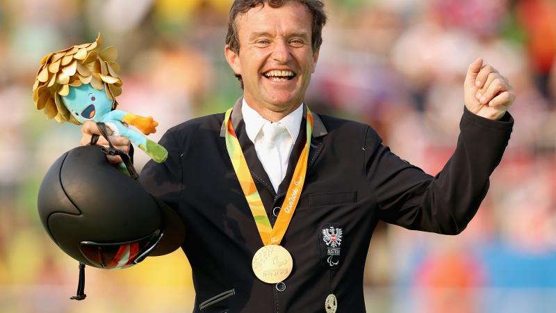 male Para equestrian rider Pepo Puch holds up his arms in celebration with a gold medal round his neck