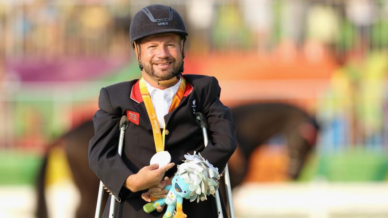 male Para equestrian rider Lee Pearson standing on crutches holding a medal