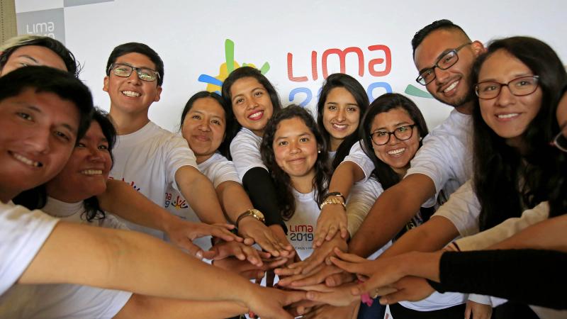 Twelve people smiling and placing their hands on each others'