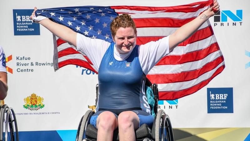 female Para rower Hallie Smith smiling and holding up a USA flag