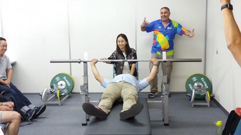 an official tries out the weight of a powerlifting bar while lying on the bench