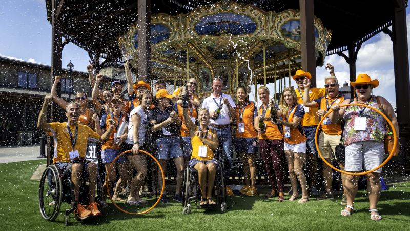 Group photo of Dutch Para equestrian team dressed in orange team colors celebrating with champagne 