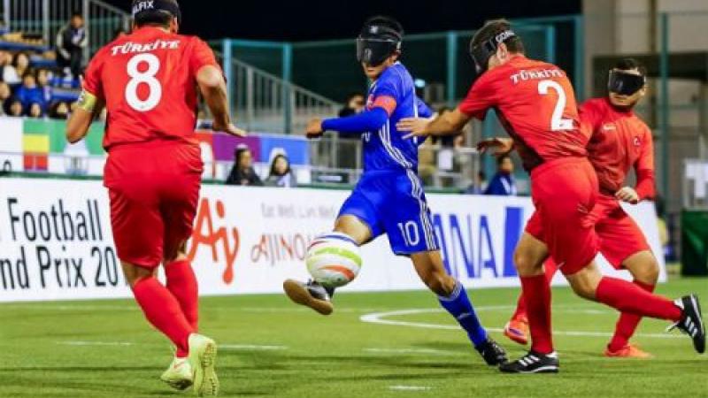 a Japanese blind footballer dribbles the ball through two opponents