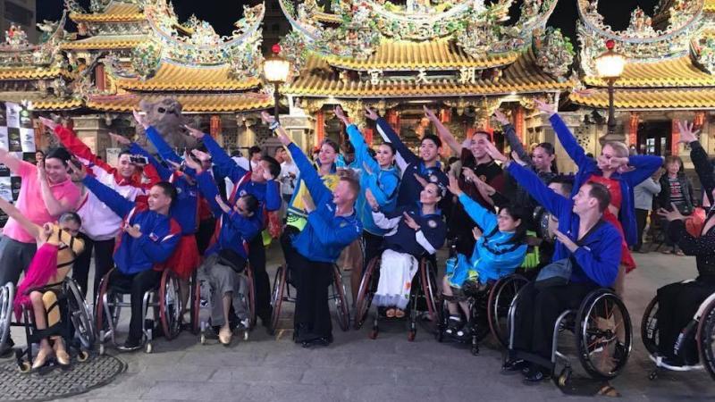 a group of Para dancers raising their arms in front of three golden Chinese temples