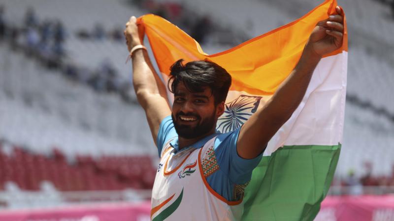 male Para athlete Sandeep Sandeep smiling and holding up an India flag