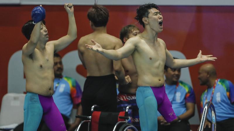 three male Para swimmers celebrate at the edge of the pool 