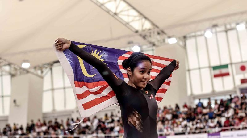 female Para cyclist Nur Azlia Syafinaz Mohd Zais holds up a Malaysia flag