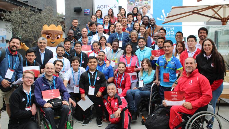 a group of people and the Lima 2019 mascot smile for a photo