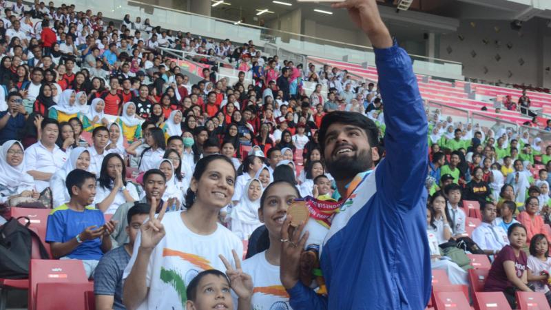 Man with a medal taking pictures with fans on the stands in a stadium