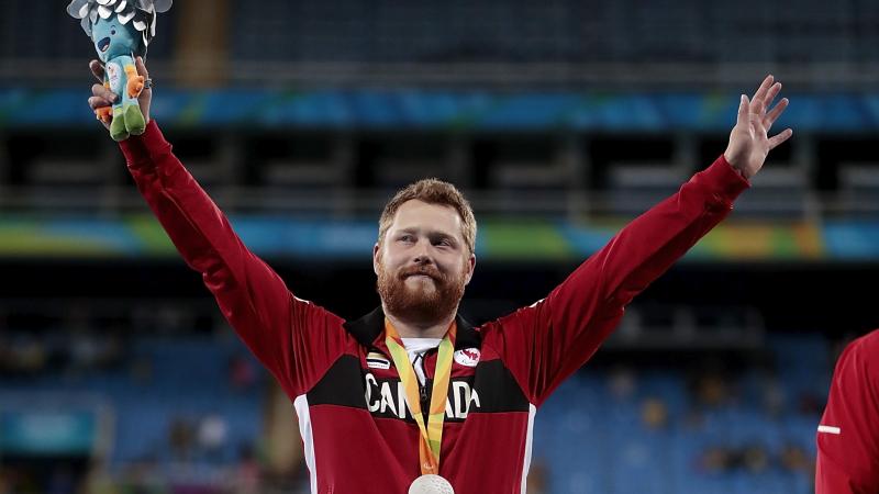 male Para athlete Alister McQueen raises his arms on the podium