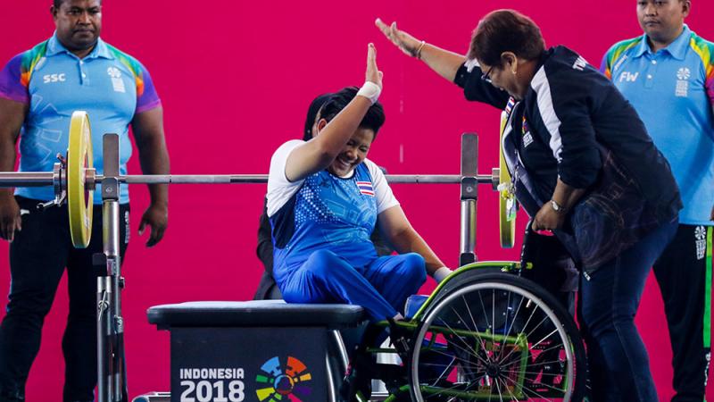 Woman powerlifter on a bench celebrating with another woman