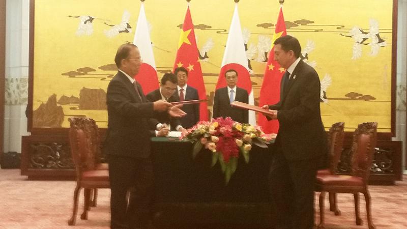 Beijing 2022 and Tokyo 2020 men in suits in a room exchanging documents