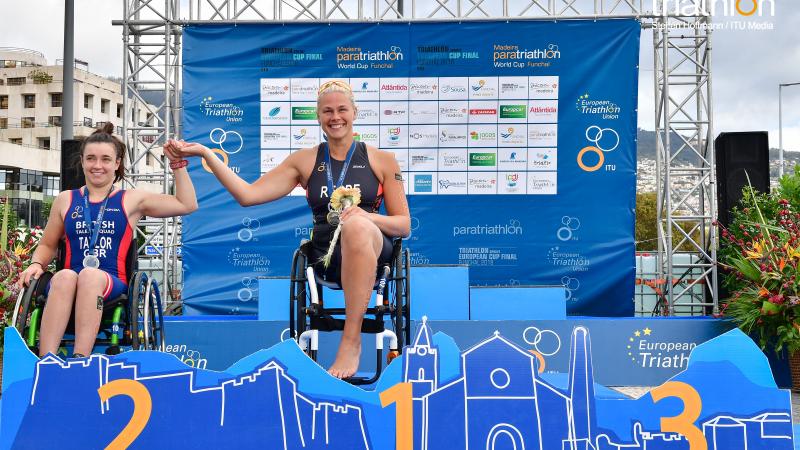 female Para triathlete Christiane Reppe holds the hand of another female athlete on the podium