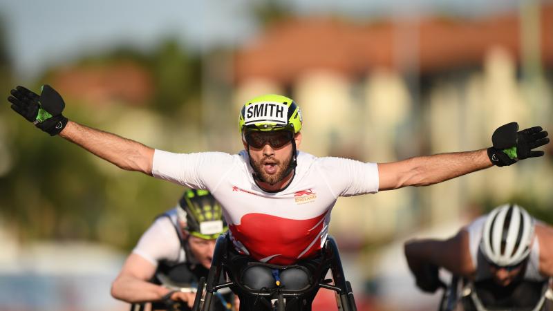 male wheelchair racer Johnboy Smith raises his arms wide as he crosses the finish line