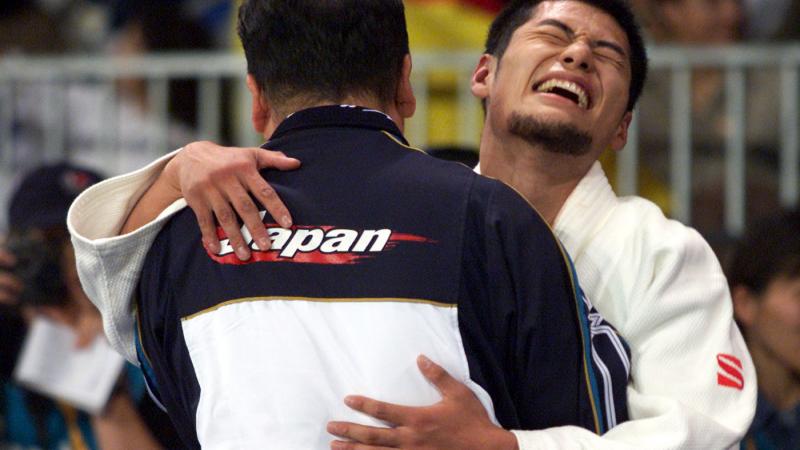 male judoka Satoshi Fujimoto hugs another man