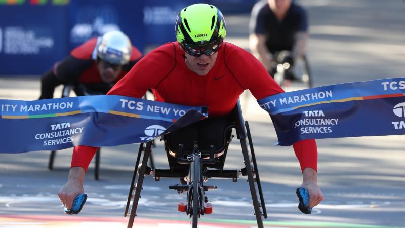male wheelchair racer Daniel Romanchuk breaks the tape on the finish line ahead of two other wheelchair racers