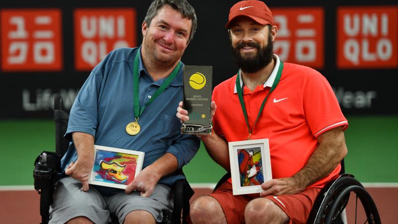 Two men in wheelchair tennis holding a trophy on a tennis court