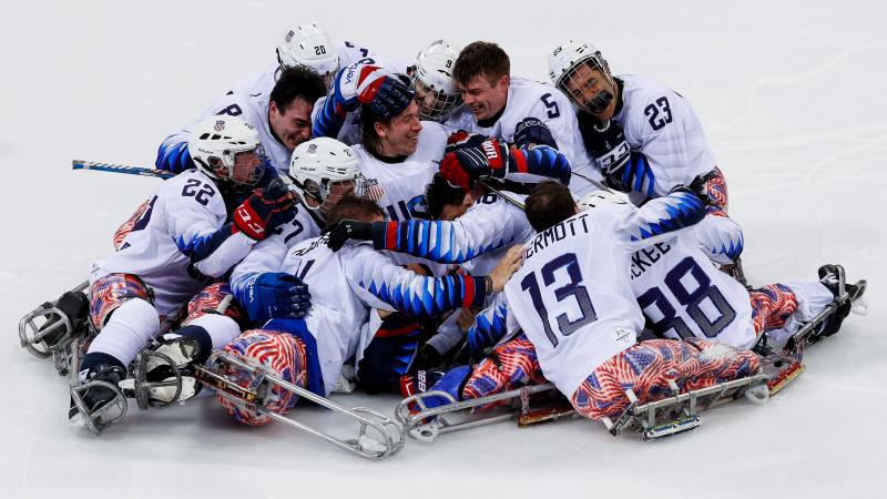 male USA ice hockey players celebrate hugigng in a big group on the ice