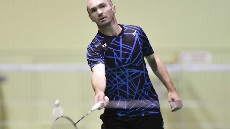 male Para badminton player Corrie Keith Robinson standing and playing a forehand shot