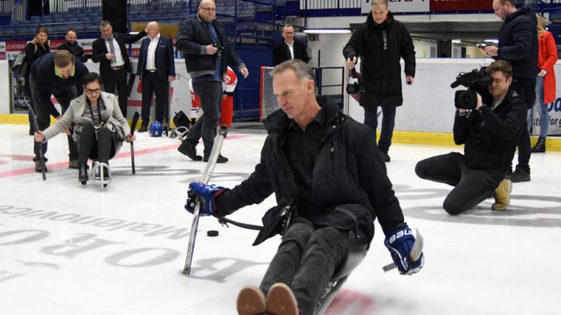 A group of people on an ice rink with a man trying Para ice hockey