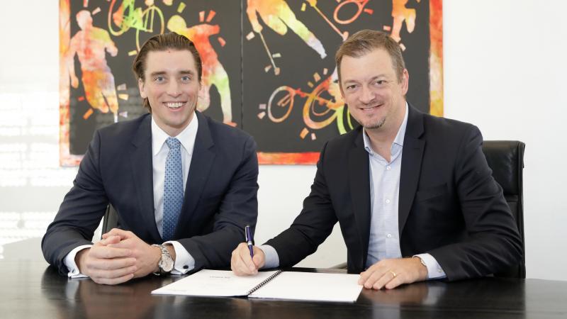 Two men smiling while one of the signs a contract