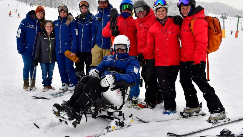 a group of skiing technical people standing behind a male Para alpine sit skier on the ski slope