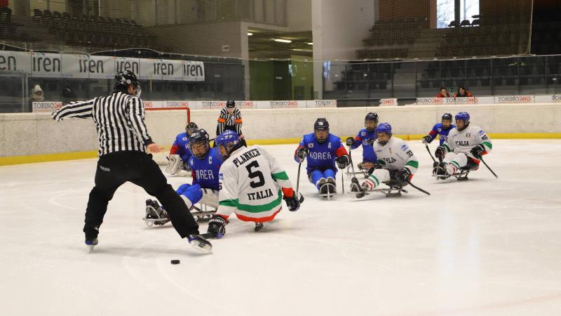 Two referees, three Italian and five South Korean Para ice hockey players on ice 