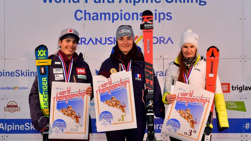 three female skiers including Marie Bochet standing on the podium holding prints