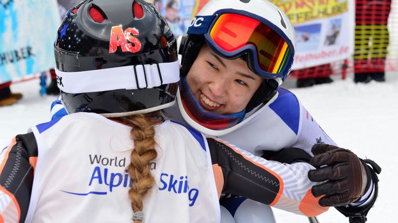 female Para alpine skier Momoka Muraoka hugs another female skier and smiles