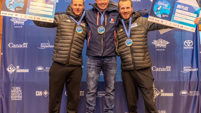 three male Para snowboarders with Maxime Montaggioni in the middle standing on the podium with their arms around eachother
