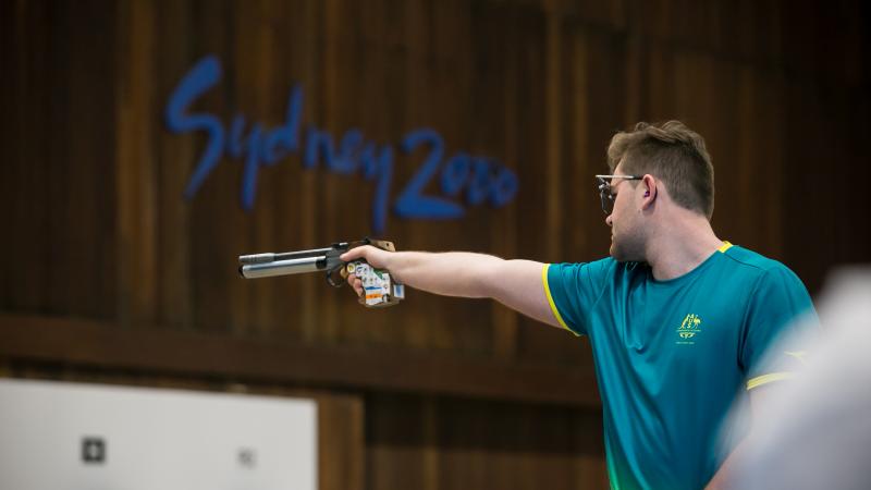 a male shooting Para sport athlete points his pistol at a target