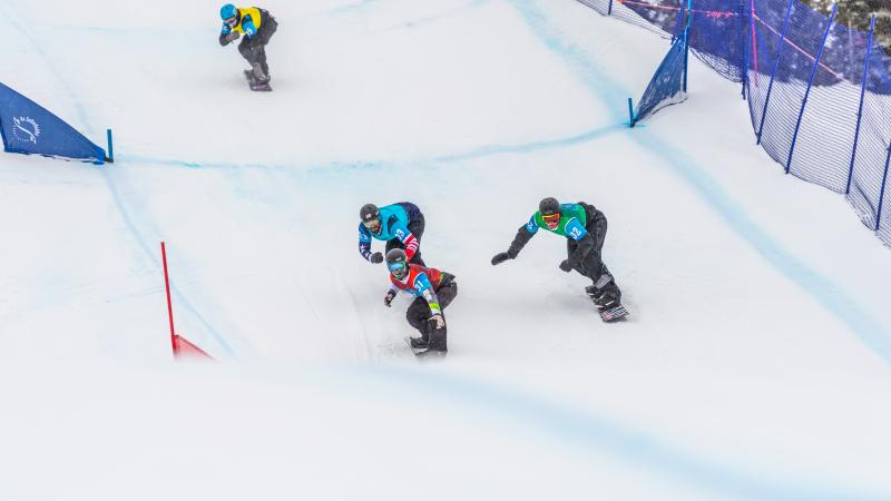 four male Para snowboarders racing on the snow with Alex Massie on the right