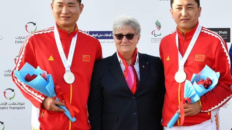 Chinese Para shooters Yang Chao and Huang Xing standing either side of a woman and smiling on the podium