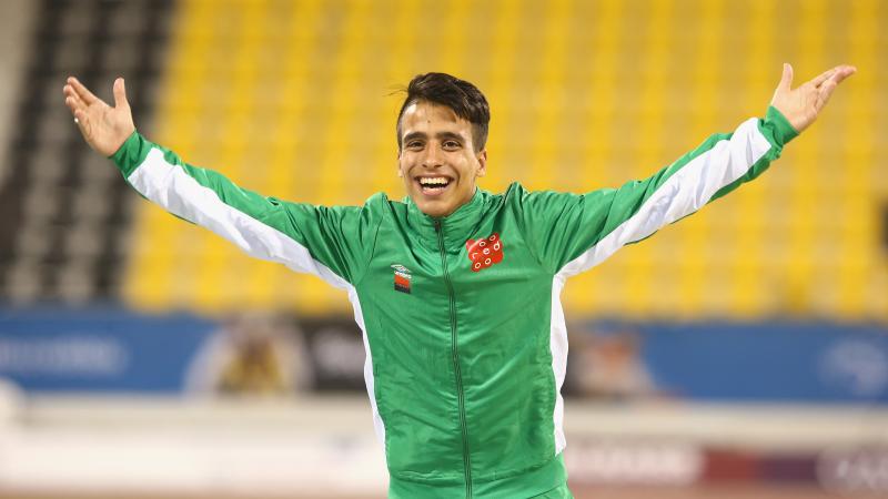 male Para athlete Abdellatif Baka raises his arms in celebration on the podium 