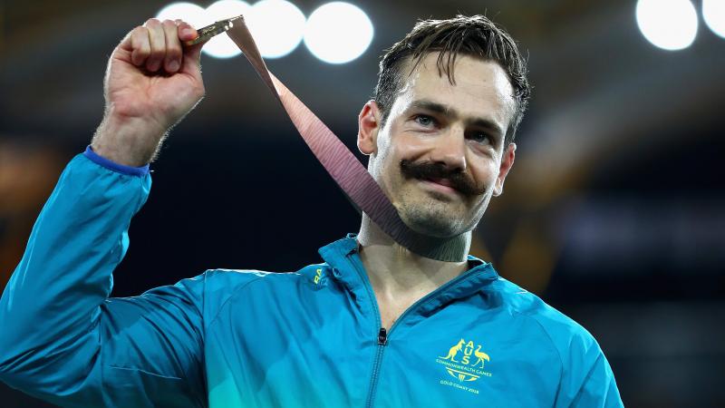 male Para sprinter Evan O'Hanlon holds up a gold medal on the podium