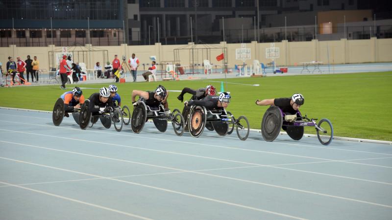 Group of men in racing chairs compete on a track