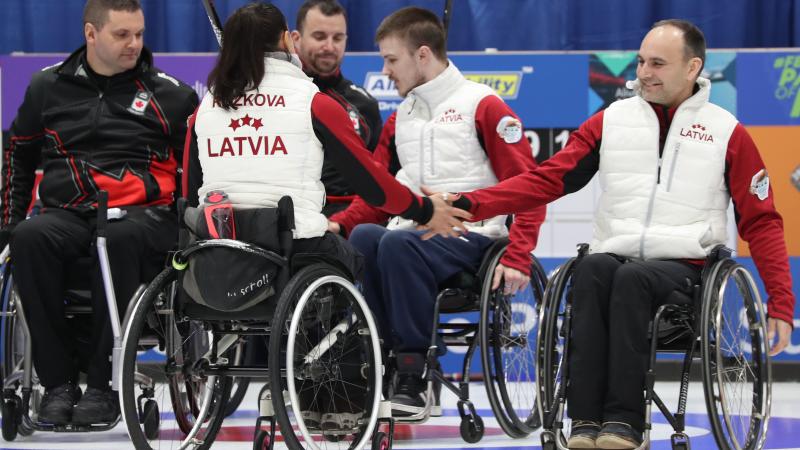 wheelchair curlers from Latvia high-five after beating Canada on the ice