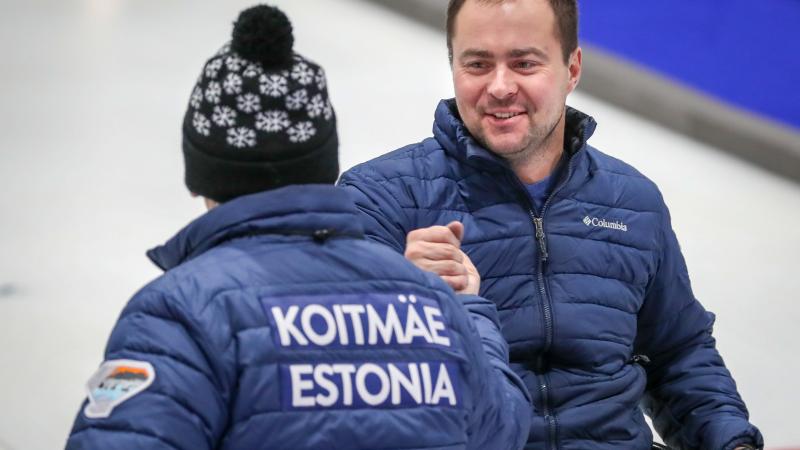 Two male wheelchair curling teammates clasp hands 