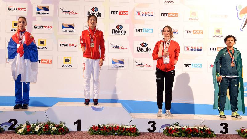 four female taekowondo fighters on the podium with Yujie Li on the top step