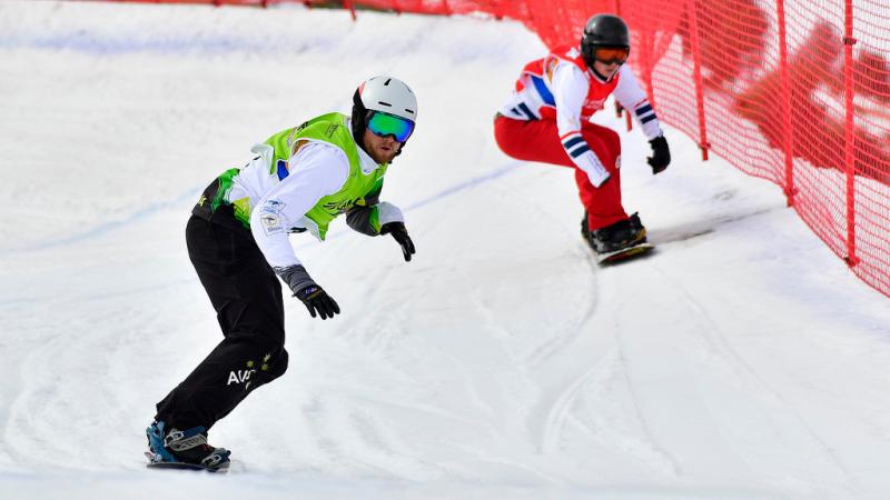 two male Para snowboarders racing down the slope head to head 