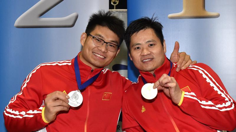 male wheelchair fencers Hu Daoliang and Feng Yanke hold up their medals and smile