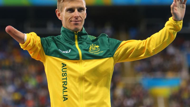 male Para athlete Michael Roeger raises his arms on the podium