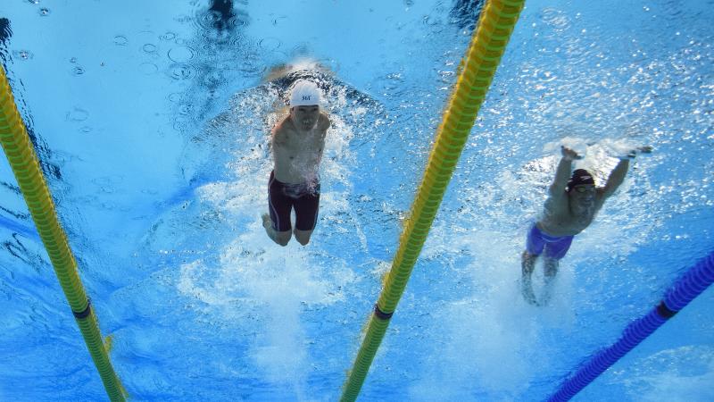 An armless man swimming next to a short stature man